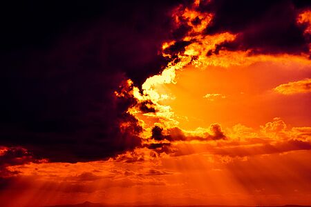 Ein dramatisch wirkender Sonnenuntergang. Der Himmel ist tief orange, die Sonne steht hinter einer dunklen Wolke