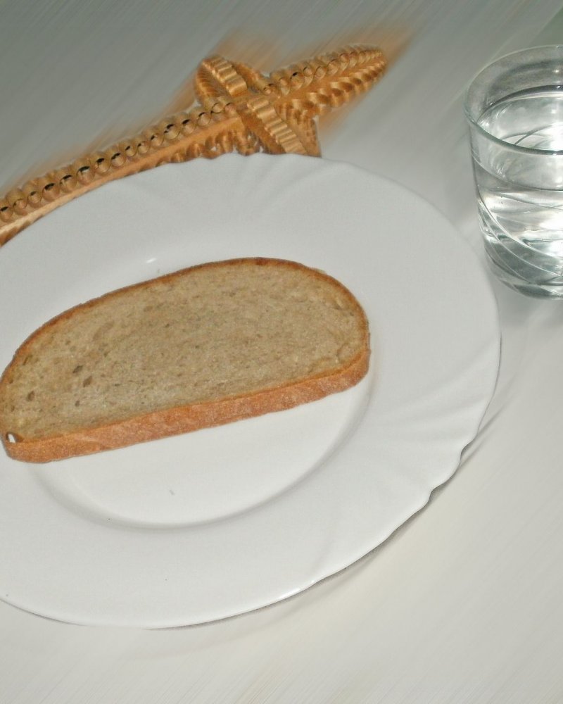 Teller mit Brotscheibe, Glas Wasser und Kreuz